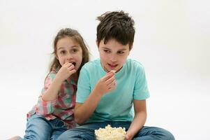 contento bambini, ragazzo e ragazza mangiare Popcorn, Guardando film, sorridente guardare a telecamera, isolato su bianca studio sfondo foto