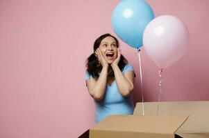 emotivo incinta donna esprimendo contento sorpresa mentre rosa e blu palloncini appare a partire dal un' scatola, aspettandosi Gemelli. foto