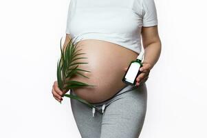 avvicinamento gravido donna Tenere palma foglia e cosmetico olio massaggio per ridurre o impedire allungare votazione a gravidanza volta, foto