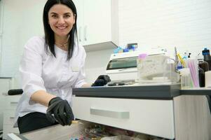 bellissimo femmina dentista medico, dentale igienista, ortodontista Lavorando nel dentale ufficio, sorridente guardare a telecamera foto