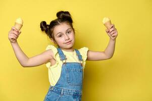 adorabile poco ragazza Tenere cialda cono con scoop di delizioso ghiaccio crema, guardare a telecamera, al di sopra di giallo fondale foto