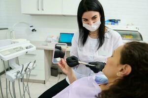 dentista medico Tenere denti colore grafico, discutere con paziente il denti protesi e candeggio nel odontoiatria clinica foto