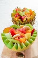 due macedonie di frutta fresca con kiwi, banana, pesca, arancia, arancia rossa, albicocca e melone in una ciotola di melone e ananas fatta a mano. foto
