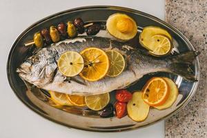 orata pesce alla piastra al forno con patate, rosmarino, limone, arancia, olive, pomodori e lime. orata fresca, preparazione di pesce dorade. foto