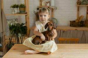 un' poco contento ragazza giocando con un' bassotto cane nel il cucina foto