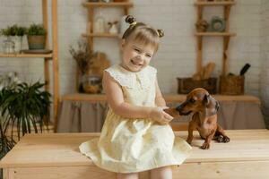 un' poco contento ragazza giocando con un' bassotto cane nel il cucina foto