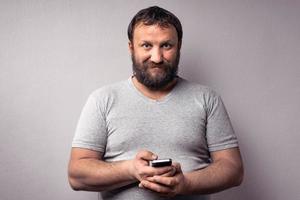 uomo barbuto in maglietta grigia che tiene il cellulare foto