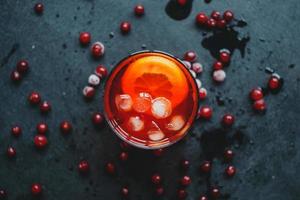 aperol spritz con ghiaccio e mirtilli rossi su sfondo nero.
