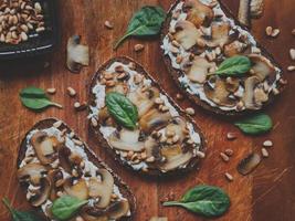 gustosa bruschetta fresca con funghi, spinaci, aglio, crema di formaggio e pinoli, su una tavola di legno, su uno sfondo scuro. foto