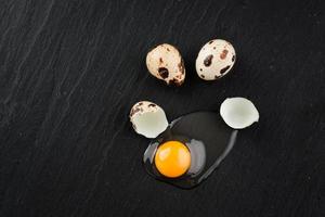 uova di quaglia su sfondo di pietra nera, uovo di quaglia rotto e incrinato, tuorlo d'uovo di quaglia. prodotto biologico. foto