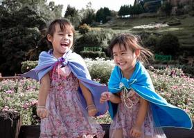 due bambine nello scialle giocano al supereroe sorridono felicemente in giardino.