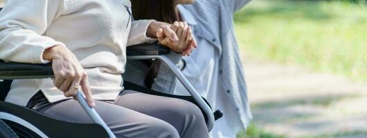 asiatico anziano donna nel sedia a rotelle con contento figlia. famiglia relazione pensionato donna seduta su sedia a rotelle nel il parco età cura a la pensione casa. foto