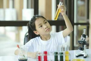 poco ragazza nel sollevamento e guardare a sostanza nel tubo nel chimica scienza classe. foto