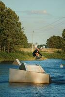 bellissimo Visualizza di giovane uomo ciclista Tenere corda e fabbricazione estremo saltare su wakeboard. wakeboard e acqua gli sport attività. Basso angolo tiro di uomo wakeboard su un' lago. uomo acqua sciare a tramonto. foto