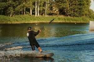 bellissimo Visualizza di giovane uomo ciclista Tenere corda e fabbricazione estremo saltare su wakeboard. wakeboard e acqua gli sport attività. Basso angolo tiro di uomo wakeboard su un' lago. uomo acqua sciare a tramonto. foto