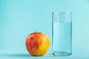 mela e bicchiere di acqua pura su sfondo blu. concetto di cibo salutare e dietetico foto