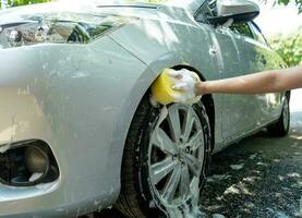 mani di asiatico donna Tenere giallo spugna, lavaggio auto ruota con schiuma. foto