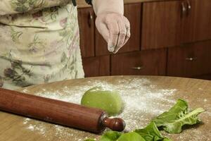 nonna mani impasto verde Impasto per tagliatelle nel il cucina. foto