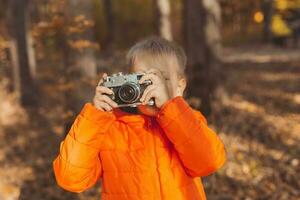 ragazzo con retrò telecamera assunzione immagini all'aperto nel autunno natura. tempo libero e fotografi concetto foto