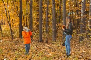 ragazzo fotografo prende immagini di un' madre nel il parco nel autunno. hobby, foto arte e tempo libero concetto.