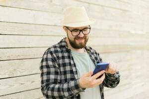 sorridente maschio turista uso smartphone durante estate città rompere al di sopra di di legno parete - tecnologie e sociale media App concetto foto