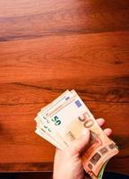 la mano tiene una pila di cinquanta banconote in euro sullo sfondo della tavola in legno. salario e stipendio minimo in europa union. foto