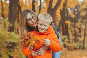 madre abbracciare sua bambino durante camminare nel autunno parco. autunno stagione e singolo genitore concetto. foto