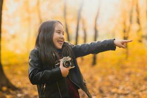 bambino ragazza utilizzando un vecchio stile telecamera nel autunno natura. fotografo, autunno stagione e tempo libero concetto. foto