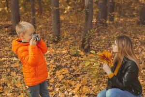 ragazzo fotografo prende immagini di un' madre nel il parco nel autunno. hobby, foto arte e tempo libero concetto.