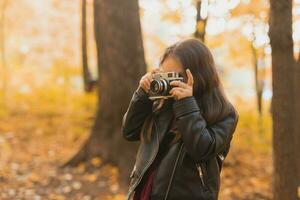 bambino ragazza utilizzando un vecchio stile telecamera nel autunno natura. fotografo, autunno stagione e tempo libero concetto. foto