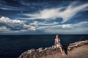 donna bionda al litorale. attraente donna bionda seduta sul muro di pietra in riva al mare. foto