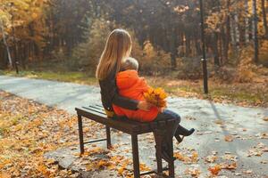 singolo genitore madre e bambino ragazzo nel il autunno nel parco sedersi su panca. autunno stagione e famiglia concetto. foto