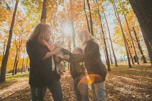 nonna e madre con nipotina avendo divertimento con cane nel autunno stagione. generazione, tempo libero e famiglia concetto foto