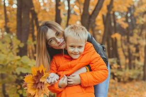 madre abbracciare sua bambino durante camminare nel autunno parco. autunno stagione e singolo genitore concetto. foto