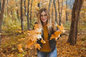 contento ridendo giovane donna lancio le foglie nel autunno parco. autunno stagione foto