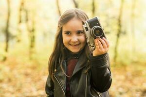 bambino ragazza utilizzando un vecchio stile telecamera nel autunno natura. fotografo, autunno stagione e tempo libero concetto. foto