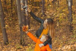 figlio e madre siamo assunzione autoscatto su telecamera nel autunno parco. singolo genitore, tempo libero e autunno stagione concetto. foto