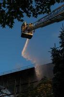 vigili del fuoco che salgono la scala contro la costruzione e l'estinzione di un incendio foto