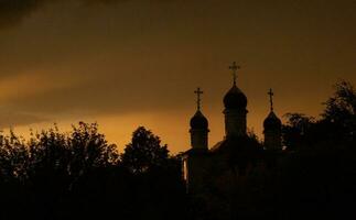 il silhouette di il cupole di un ortodosso cristiano Chiesa nel Romania contro il sfondo di il rosso cielo. fede o religione concetto foto