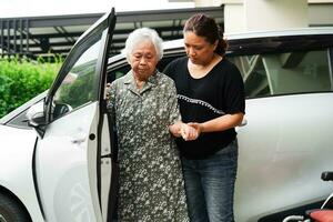il caregiver aiuta il paziente con disabilità della donna anziana asiatica a salire nella sua macchina, concetto medico. foto