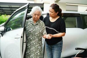 il caregiver aiuta il paziente con disabilità della donna anziana asiatica a salire nella sua macchina, concetto medico. foto