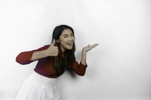 eccitato asiatico donna indossare rosso maglietta, puntamento a il copia spazio accanto suo, isolato di bianca sfondo foto