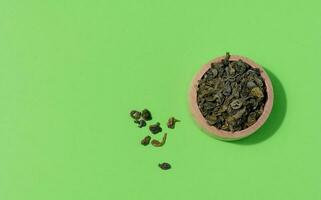 asciutto lanciato verde tè nel un' di legno ciotola su un' verde sfondo, superiore Visualizza foto