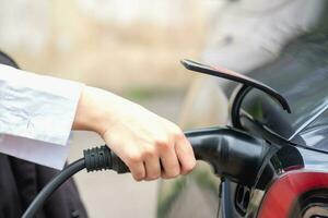 elettrico auto o ev ricarica stazione un' donna spine nel un' nero energia cavo per caricare per pulito energia per un' viaggio eco concetto e pulito energia con elettrico veicolo tecnologia. foto