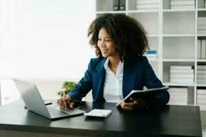 africano donna libero professionista è Lavorando sua lavoro su computer tavoletta e il computer portatile fare contabilità analisi rapporto vero tenuta investimento dati, finanziario a ufficio foto