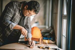 asiatico falegname Lavorando con attrezzatura utensili su di legno tavolo nel carpenteria negozio. concetto Lavorando di falegname. professionale Lavorando di legno uomo. foto