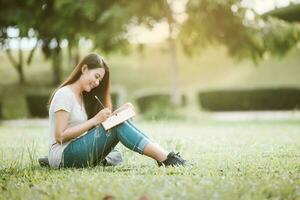 contento donna alunno seduta a parco e scrittura qualcosa su taccuino, formazione scolastica concetto foto