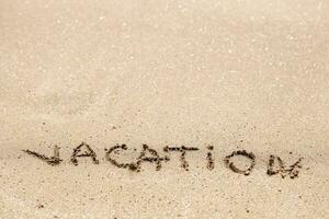 parola vacanza scritto su il sabbia foto