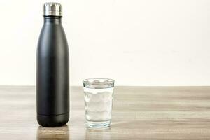 riutilizzabile bottiglia e bicchiere di acqua su di legno tavolo. foto