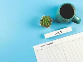 piatto posare di abitudine inseguitore libro con di legno calendario dicembre, blu tazza di nero caffè e succulento pianta pentola su blu sfondo con copia spazio. foto